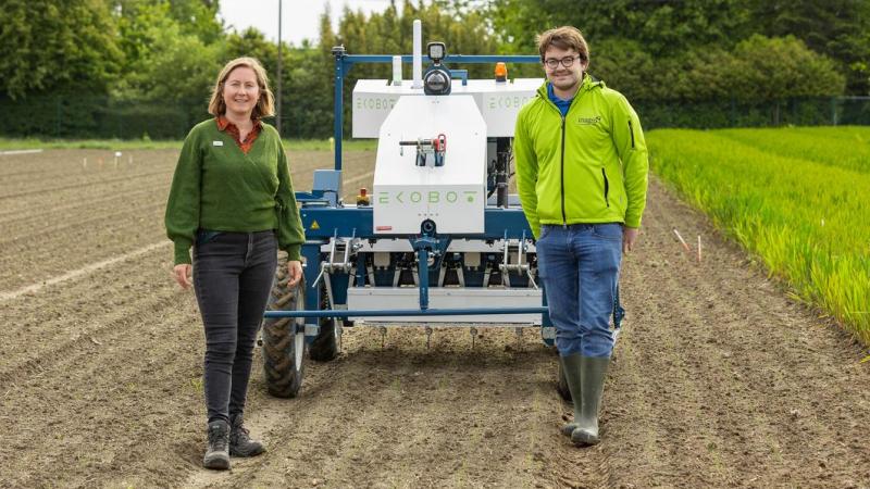 Eva Ampe en Robbe Moens, onderzoekers precisielandbouw bij Inagro, naast de Ekobot. Deze robot verwijdert onkruid met kleine u-vormige schepjes.