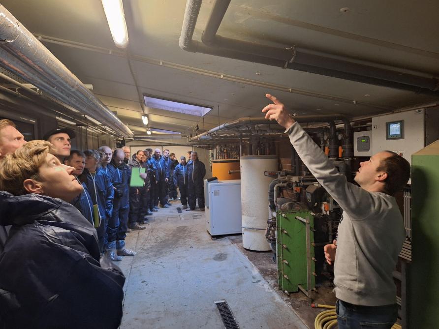 Brecht D’heygere toont het koeldeksysteem op de varkenshouderij. Onder andere de warmtepomp is te zien op de achtergrond.