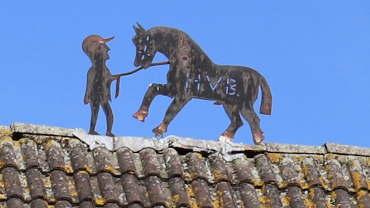 De metalen nokversiering boven het woonhuis en aanpalende stalling bestaat uit een afbeelding van een hengst en zijn begeleider met de initialen ‘HVB’. Die verwijzen naar de intussen 88-jarige Hendrik Van Brempt.