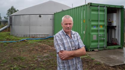 Paul Leenaerts bij de vergister: groene container (met motoren, warmtewisselaar, filters,…), reactor (grijze silo) en uiterst links daarvan een buis die schuim leidt naar een put die dienst doet als schuimopvang.