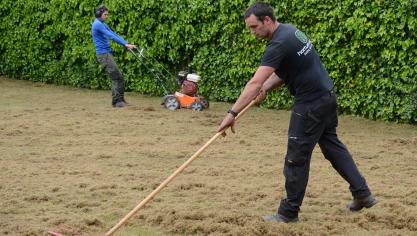 Wilhelm Desmyter aan het werk met de hark na het maaien. Op de achtergrond helper Mateo Godefroid met de grasmachine.