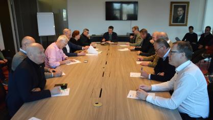 Rond de tafel zitten 6 vertegenwoordigers van de pluimveehouders en 6 vertegenwoordigers van de verwerkers en handelaren, met 1 ambtenaar als scheidsrechter.
