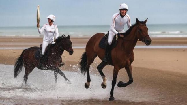 Pénélope Leprévost met de Olympische vlam en Nicolas Canteloup in galop op Omaha Beach.