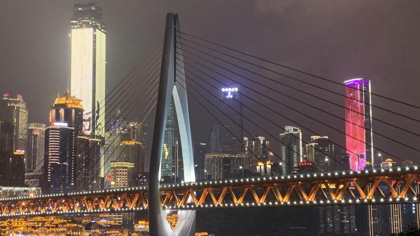 Zicht op Chongqing-stad by night. De stad is gelegen aan de samenvloeiing van de Yangtze en de Jialing. Een wervelend geheel van wolkenkrabbers die in hoogte en uitbundige verlichting rivaliseren en symbool staan voor de megapool met maat XXL, waarvan het hart 24 op 24 uur in een dolle koers blijft slaan.