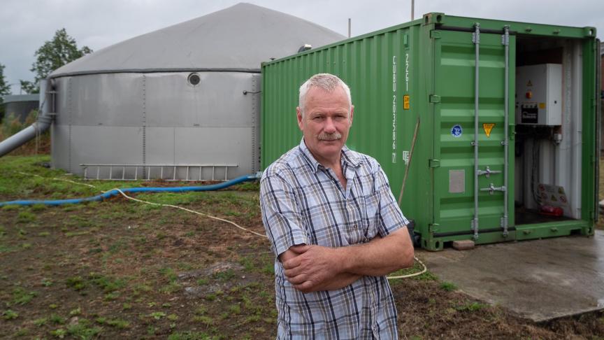 Paul Leenaerts bij de vergister: groene container (met motoren, warmtewisselaar, filters,…), reactor (grijze silo) en uiterst links daarvan een buis die schuim leidt naar een put die dienst doet als schuimopvang.